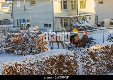 Winterszene mit Pferdeschlitten, auf der der Weihnachtsmann mit einer Tasche voller Geschenke entlang der Straße zwischen Villen fährt. Schweden. Stockfoto