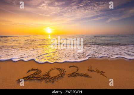 Happy New Year 2024 Konzept, Schriftzug am Strand. Geschriebener Text am Strand bei Sonnenaufgang. Stockfoto