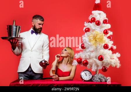 Frohe Weihnachten und frohes neues Jahr. Romantisches Abendessen im Restaurant. Kellner mit einer Flasche Champagner in Eiskübel und Tablett. Geschenk und Überraschung für Stockfoto