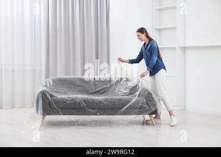 Junge Frau, die Plastikfolie zu Hause vom Sofa weglegt Stockfoto