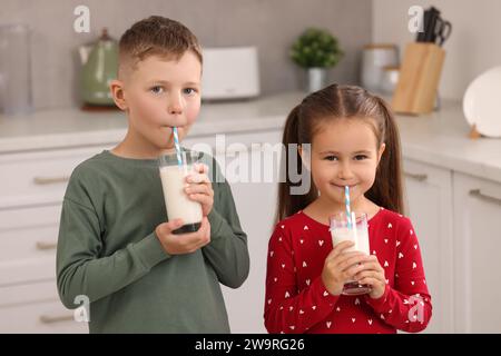 Süße Kinder, die frische Milch aus Gläsern in der Küche trinken Stockfoto