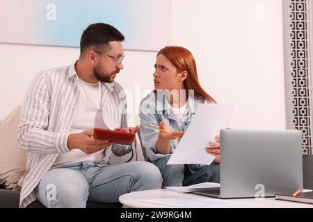 Emotionales Paar berechnet Steuern am Tisch im Wohnzimmer Stockfoto