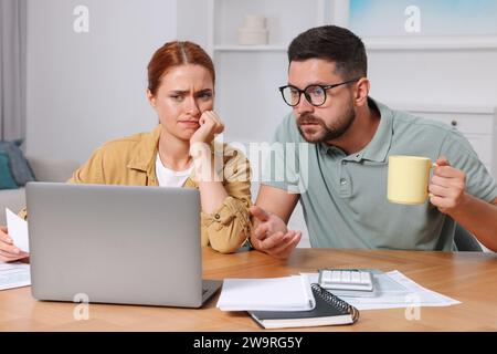 Emotionales Paar, das Steuern am Tisch im Zimmer macht Stockfoto