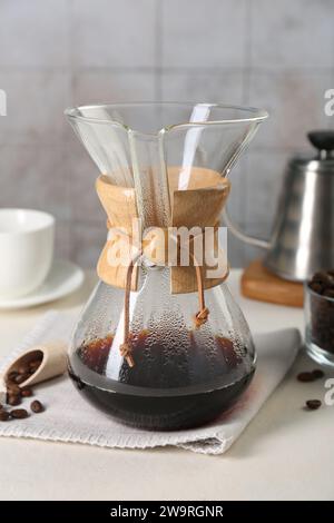 chemex-Glaskaffeemaschine mit leckerem Tropfkaffee und Bohnen auf weißem Tisch Stockfoto