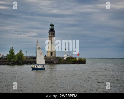 Ein Segelboot, das an einem bewölkten Septembertag vor dem Leuchtturm von Buffalo Main Light an der Marina vorbeifährt. Stockfoto