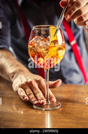 Der Barkeeper in der Bar bereitet den Sommer-Cocktail Spritz Veneziano zu und fügt dem Getränk eine Scheibe Orange hinzu. Stockfoto