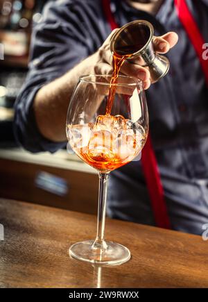 Der Barkeeper in der Bar bereitet einen Sommer-Cocktail Spritz Veneziano zu und gießt Aperol Likör in ein Glas mit Eis. Stockfoto