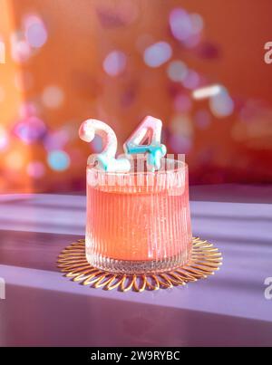 24. Geburtstag Zahlen in einem Cocktailglas, 2024 NYE Celebration Cocktail, 24 Jahre, 24. Jahrestag auf Einem festlichen Bokeh Hintergrund in Orange Stockfoto