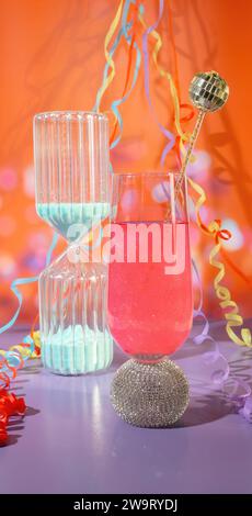 Ein Sandtimer Countdown und ein Glas Pink Celebration mit glitzerndem Champagner mit Partyströmen und Konfetti, NeujahrsCountdown Stockfoto