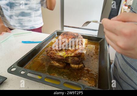 Gebratene Lammschulter auf dem Küchentisch. Hände halten die Gabel und kontrollieren das Lamm. Hausmannskost und Unterhaltung. Stockfoto