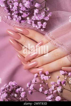 Weibliche Hände mit schöner Maniküre mit Gipsofila-Blüten auf rosa Seide Stockfoto