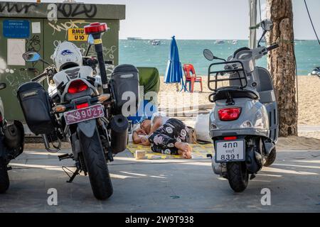 Eine asiatische Obdachlose wird zwischen zwei Rollern, darunter einer von der Polizeiwache, am Pattaya Beach schlafen gesehen. Pattaya Beach ist ein bekanntes Touristenziel in Thailand. Pattaya City hat sich zwar einen Ruf für sein pulsierendes Nachtleben und seine Unterhaltungsmöglichkeiten erworben, aber es konzentriert sich nicht nur auf männliche Alleinreisende. Neben dem Nachtleben zieht die Stadt zahlreiche Touristen an, darunter Familien, Paare und Einzelpersonen jeden Alters, um einkaufen zu gehen, Wasseraktivitäten zu Unternehmen und sich am Meer zu entspannen. (Foto: Nathalie Jamois/SOPA Images/SIPA USA) Stockfoto