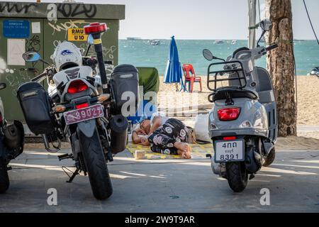 Pattaya, Thailand. Dezember 2023. Eine asiatische Obdachlose wird zwischen zwei Rollern, darunter einer von der Polizeiwache, am Pattaya Beach schlafen gesehen. Pattaya Beach ist ein bekanntes Touristenziel in Thailand. Pattaya City hat sich zwar einen Ruf für sein pulsierendes Nachtleben und seine Unterhaltungsmöglichkeiten erworben, aber es konzentriert sich nicht nur auf männliche Alleinreisende. Neben dem Nachtleben zieht die Stadt zahlreiche Touristen an, darunter Familien, Paare und Einzelpersonen jeden Alters, um einkaufen zu gehen, Wasseraktivitäten zu Unternehmen und sich am Meer zu entspannen. Quelle: SOPA Images Limited/Alamy Live News Stockfoto