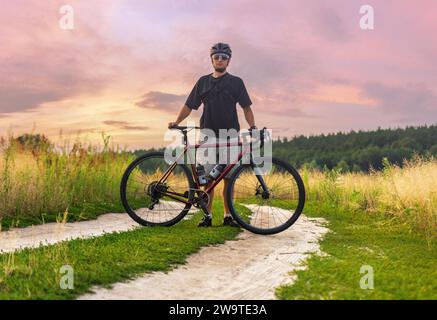 Radfahrer stehend mit seinem Schotterrad während des Sporttrainings im Freien bei Sonnenuntergang. Aktiver Lebensstil. Stockfoto