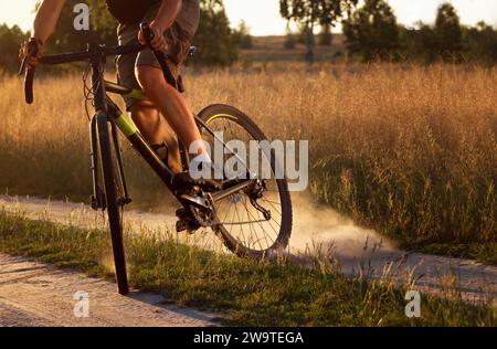 Radfahrer auf einem Feld bei Sonnenuntergang. Ein junger, sportlicher Kerl auf einem Fahrrad hebt Staub vom Hinterrad nach einem Rutschen auf. Nahaufnahme. Stockfoto