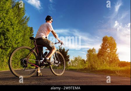 Radfahrer stehen bei Sonnenuntergang auf der Straße. Wunderschöne Landschaft eines Mannes mit Rennrad vor dem blauen Himmel. Sportlicher Lifestyle. Stockfoto