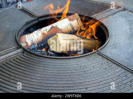 Birkenfeuerholz brennt in der Mitte eines runden Grilltisches aus Metall Stockfoto