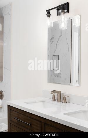 Ein Wasserhahn im Badezimmer mit einem bronzenen Wasserhahn, einer Arbeitsfläche aus weißem Marmor und einem dunklen Holzschrank. Stockfoto