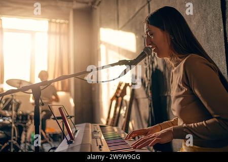 Die Sängerin spielt Synthesizer und singt im Musikstudio ins Mikrofon. Musikbandprobe. Stockfoto