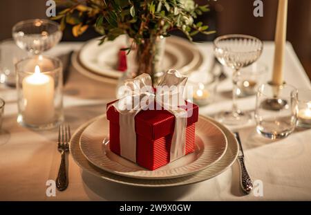 Feiertage, romantisches Datum und Festkonzept - Nahaufnahme eines festlichen Tisches für zwei Personen mit Geschenkbox, Blumen in Vase und Kerzen, die zu Hause brennen Stockfoto
