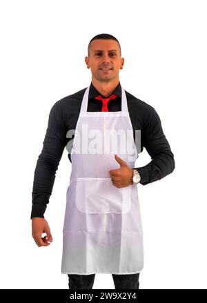 Attraktiver Koch oder Kellner posiert, trägt weiße Schürze und schwarzes Hemd isoliert auf weißem Hintergrund, im Studio-Foto, das OK-Zeichen mit Daumen nach oben macht Stockfoto