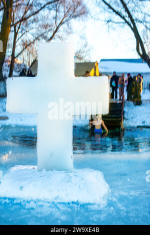 Christliches Symbol des Kreuzes, das aus einem Eisblock auf dem Eis in der Nähe eines Eislochs in einem gefrorenen See während des orthodoxen Feiertags der Epiphanik gebildet wurde Stockfoto