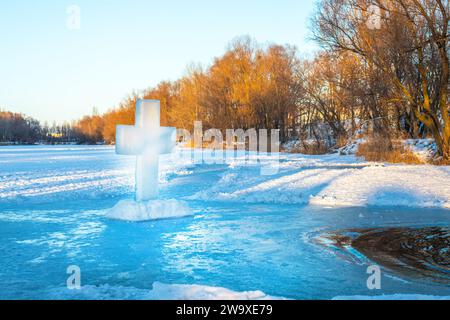 Christliches Symbol des Kreuzes, das aus einem Eisblock auf dem Eis in der Nähe eines Eislochs in einem gefrorenen See während des orthodoxen Feiertags der Epiphanik gebildet wurde Stockfoto