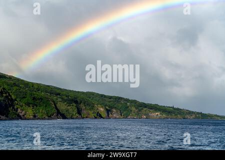 Ein leuchtender Regenbogen erstreckt sich über den Himmel über den Küstenklippen des Haleakalā-Nationalparks, von der Piilani-Autobahn auf Maui aus gesehen. Stockfoto