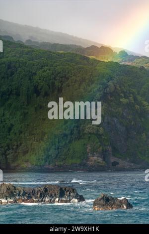 Ein lebhafter Regenbogen erhebt sich dramatisch über dem Pazifik und erreicht die wilde Küste des Haleakalā-Nationalparks, von der Piilani-Autobahn aus gesehen Stockfoto