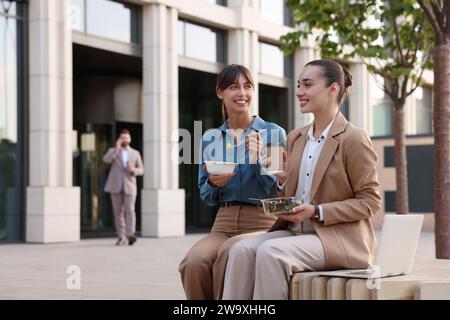 Glückliche Geschäftsfrauen, die draußen auf der Bank essen Stockfoto