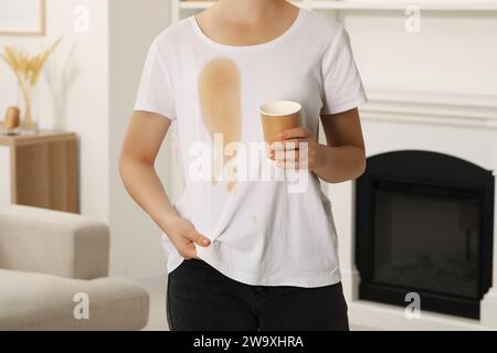 Frau zeigt Flecken von Kaffee auf ihrem Hemd drinnen, Nahaufnahme Stockfoto