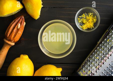 Frisch gepresster Zitronensaft und Zitronenschale mit Küchenutensilien: Frischer Zitronensaft und Zitronenschale mit Zitronen, Zitrusreibe und Kastenreibe Stockfoto