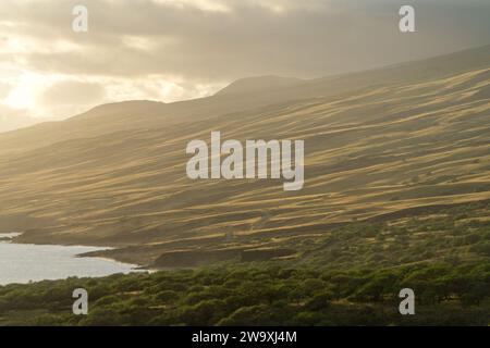 Der Piilani Highway von Maui bietet einen atemberaubenden Blick auf die von der Sonne geküssten Hügel und den Pazifischen Ozean, der von den warmen goldenen Tönen der untergehenden Sonne hervorgehoben wird. Stockfoto