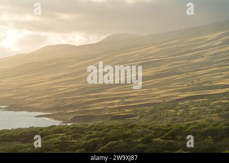 Der Piilani Highway von Maui bietet einen atemberaubenden Blick auf die von der Sonne geküssten Hügel und den Pazifischen Ozean, der von den warmen goldenen Tönen der untergehenden Sonne hervorgehoben wird. Stockfoto