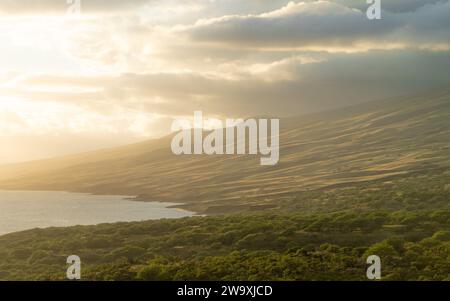 Der Piilani Highway von Maui bietet einen atemberaubenden Blick auf die von der Sonne geküssten Hügel und den Pazifischen Ozean, der von den warmen goldenen Tönen der untergehenden Sonne hervorgehoben wird. Stockfoto