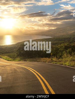 Der Piilani Highway auf Maui entfaltet sich zu einer atemberaubenden Szene, in der die untergehende Sonne einen goldenen Glanz über den Pazifik und die Insel wirft Stockfoto