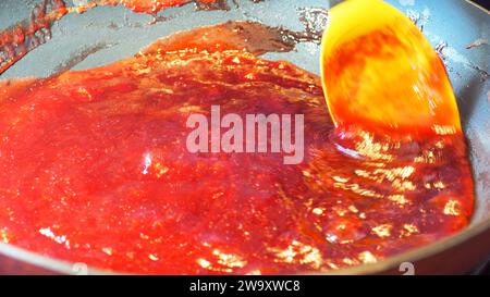 Reduzieren von Pflaumen durch langsames, kreisförmiges Rühren eines gelben Silikonlöffels Stockfoto