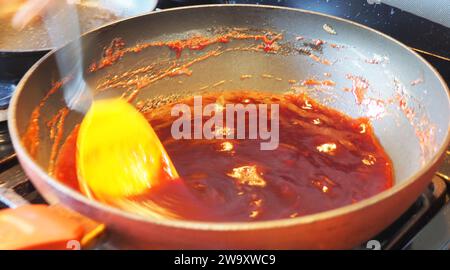 Reduzieren von Pflaumen durch langsames, kreisförmiges Rühren eines gelben Silikonlöffels Stockfoto