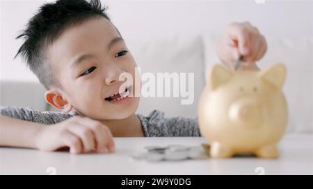 Glücklicher asiatischer Junge, der Münzen in die Schweinebank steckt Stockfoto