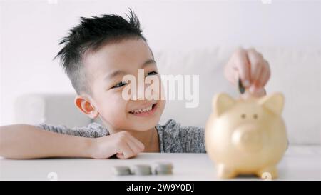 Glücklicher asiatischer Junge, der Münzen in die Schweinebank steckt Stockfoto