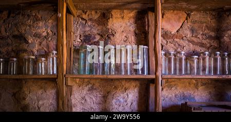 Farbige Glasgläser, die auf handgefertigten Holzregalen aufgereiht sind, sitzen an einer Steinmauer. Stockfoto