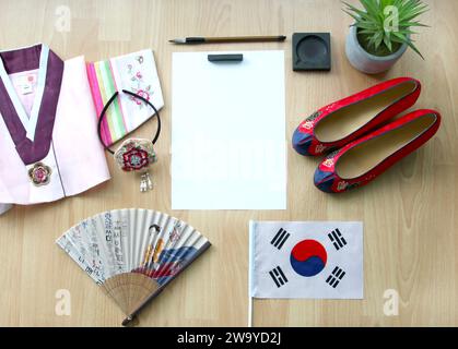 Koreanische Gomusin-Schuhe, ein Jeogori-Hanbok, Buchae-traditioneller Fan und ein Hanbok-Haarband, die südkoreanische Flagge, leeres Papier, Kalligrafiebürste und Tinte. Stockfoto