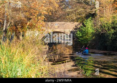 Zwei Männer paddeln im Herbst mit dem Kajak in Richtung Mytchett Place Bridge am Basingstoke Canal. Mytchett, Surrey, England, Großbritannien Stockfoto