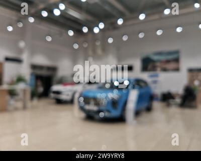 Verschwommenes neues Auto parkt im modernen Ausstellungsraum und wartet auf Verkauf. Abstrakter Hintergrund des unscharfen Platzes des Händlerbetriebs für Neufahrzeuge. Stockfoto