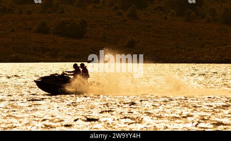 Zwei Personen, die mit einem Jet-Ski in der Silhouette vor der warmen Sommersonne fahren. Fornells Menorca Spanien. Stockfoto