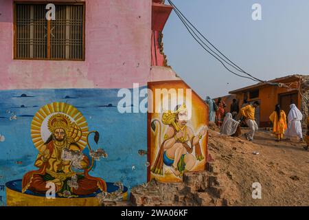 Die Menschen gehen vorbei an Wandgemälden von hinduistischen Göttern, die an den Wänden vor dem Hanuman Garhi Tempel in Ayodhya gemalt sind. Ayodhya ist eine antike Stadt in Nordindien, die im Hinduismus eine große religiöse und historische Bedeutung hat, da sie als Geburtsort von Lord Rama gilt, einer Gottheit, die in der hinduistischen Mythologie verehrt wird. Im November 2019 erließ der Supreme Court of India ein historisches Urteil für den Bau eines Hindutempels an der umstrittenen Stelle in Ayodhya. Stockfoto