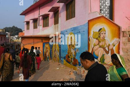 Die Menschen gehen vorbei an Wandgemälden von hinduistischen Göttern, die an den Wänden vor dem Hanuman Garhi Tempel in Ayodhya gemalt sind. Ayodhya ist eine antike Stadt in Nordindien, die im Hinduismus eine große religiöse und historische Bedeutung hat, da sie als Geburtsort von Lord Rama gilt, einer Gottheit, die in der hinduistischen Mythologie verehrt wird. Im November 2019 erließ der Supreme Court of India ein historisches Urteil für den Bau eines Hindutempels an der umstrittenen Stelle in Ayodhya. Stockfoto