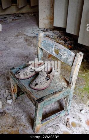 Ein abgenutzter Stuhl mit einem Paar alten Schuhen drauf, in einem baufälligen Zimmer. Stockfoto