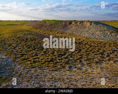 Ein Erdhügel auf einem weiten Feld, mit grünen Grasflecken unter klarem Himmel. Stockfoto