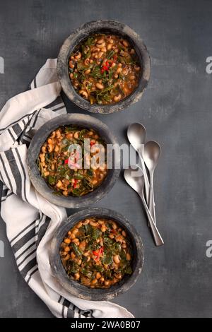 Drei Schüsseln mit veganen US Southern Blue Eye Erbsen und Kohlgrün in grauen Schüsseln, die von oben mit Kopierraum aufgenommen wurden Stockfoto